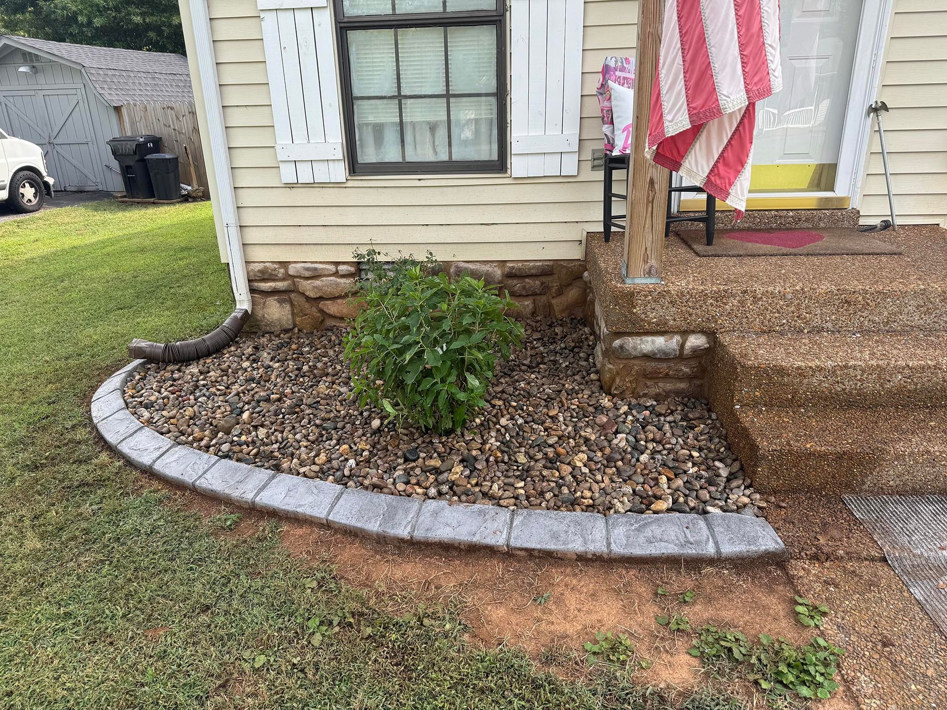 A small house with stone flowerbed edging. A bush is in the center of the rocks.