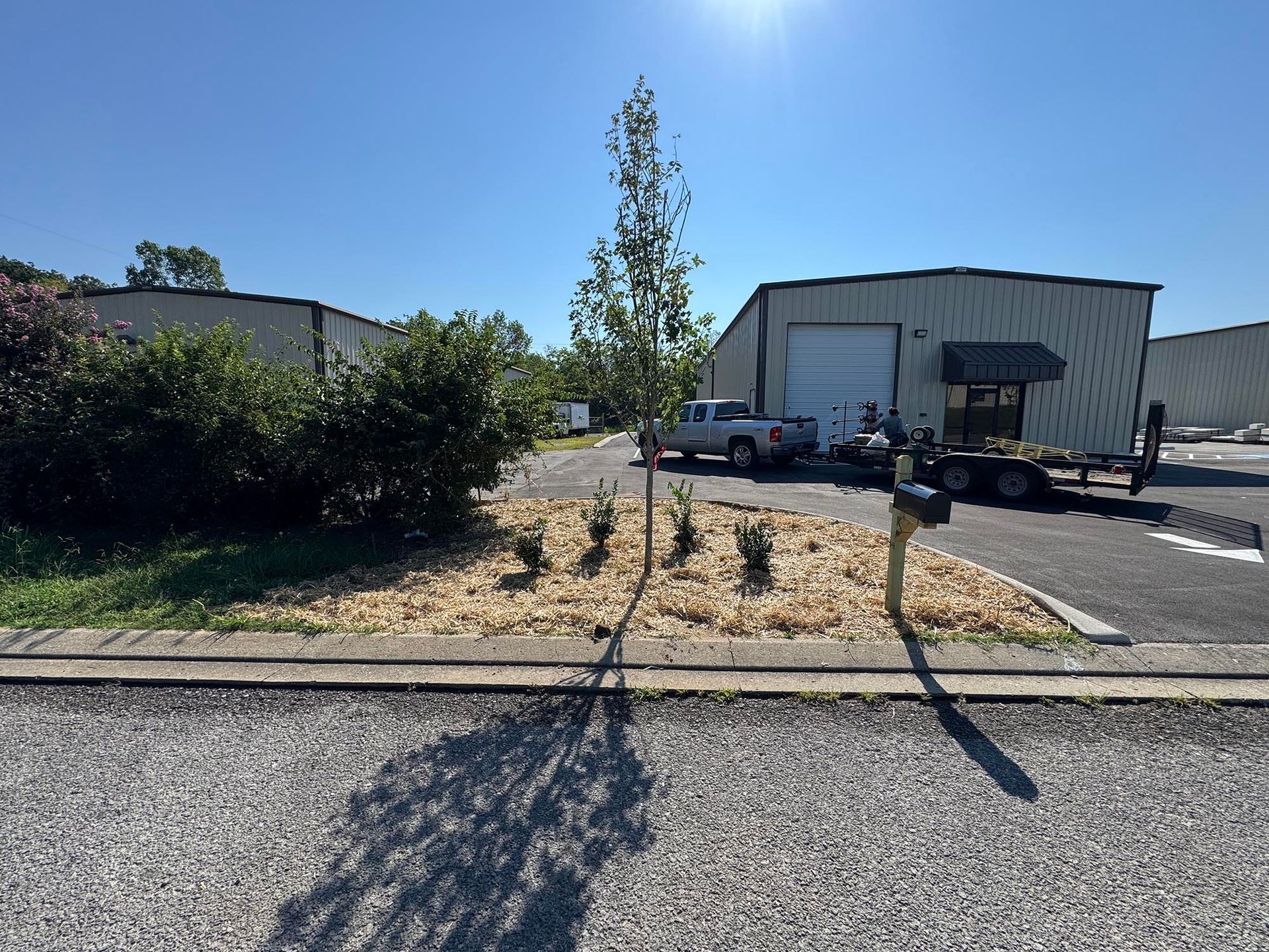 Exterior of industrial buildings with a small landscaped area, truck and trailer.