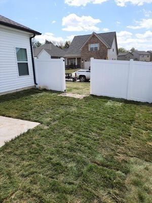 Backyard with white fence, grass, house, and truck. Sunny day with blue sky and clouds.