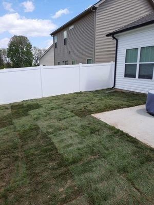 Backyard with patchy grass, white fence, patio, and two-story house on a sunny day.