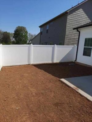 White vinyl fence encloses a bare dirt backyard next to a house with a concrete patio.