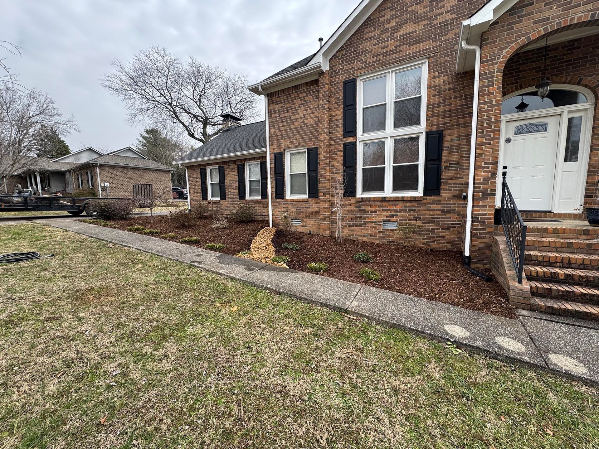 Brick house with black shutters, brown mulch, and a stone walkway.