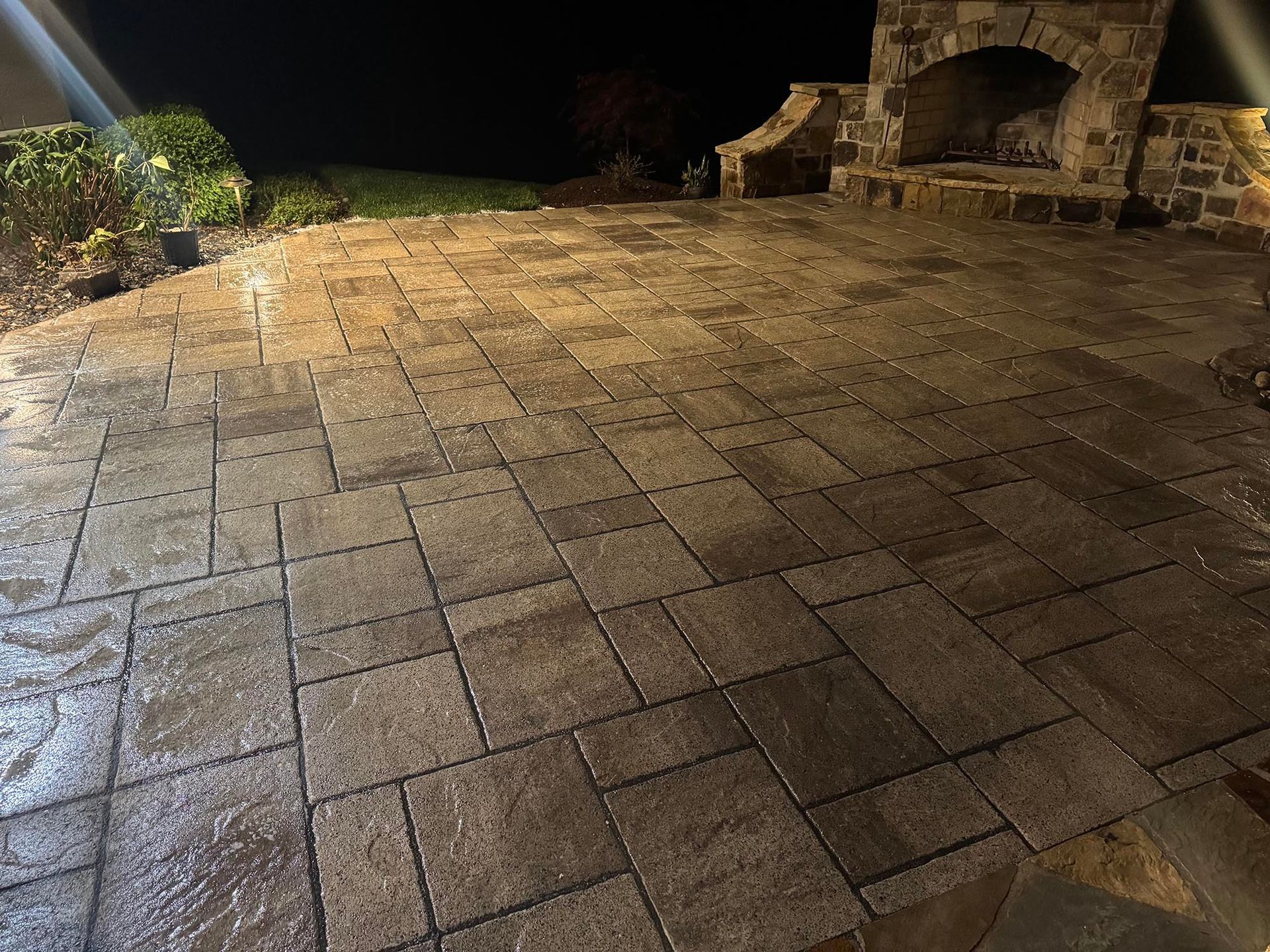 Brick patio at night with an outdoor fireplace, dark and wet.