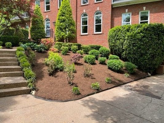 Red brick house with a landscaped hillside, bushes, trees, and stairs.