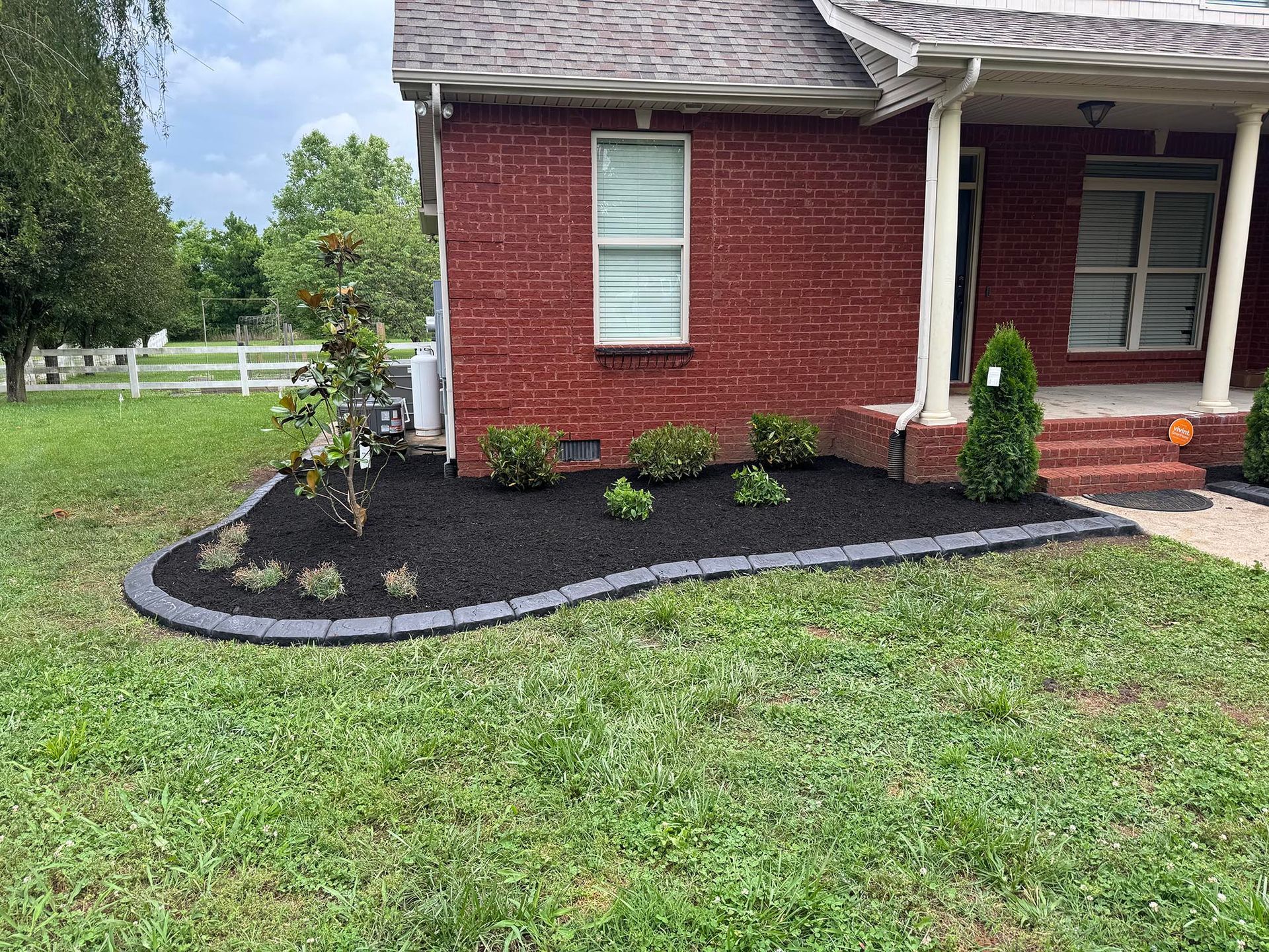 Red brick house with landscaped flower bed and green lawn.