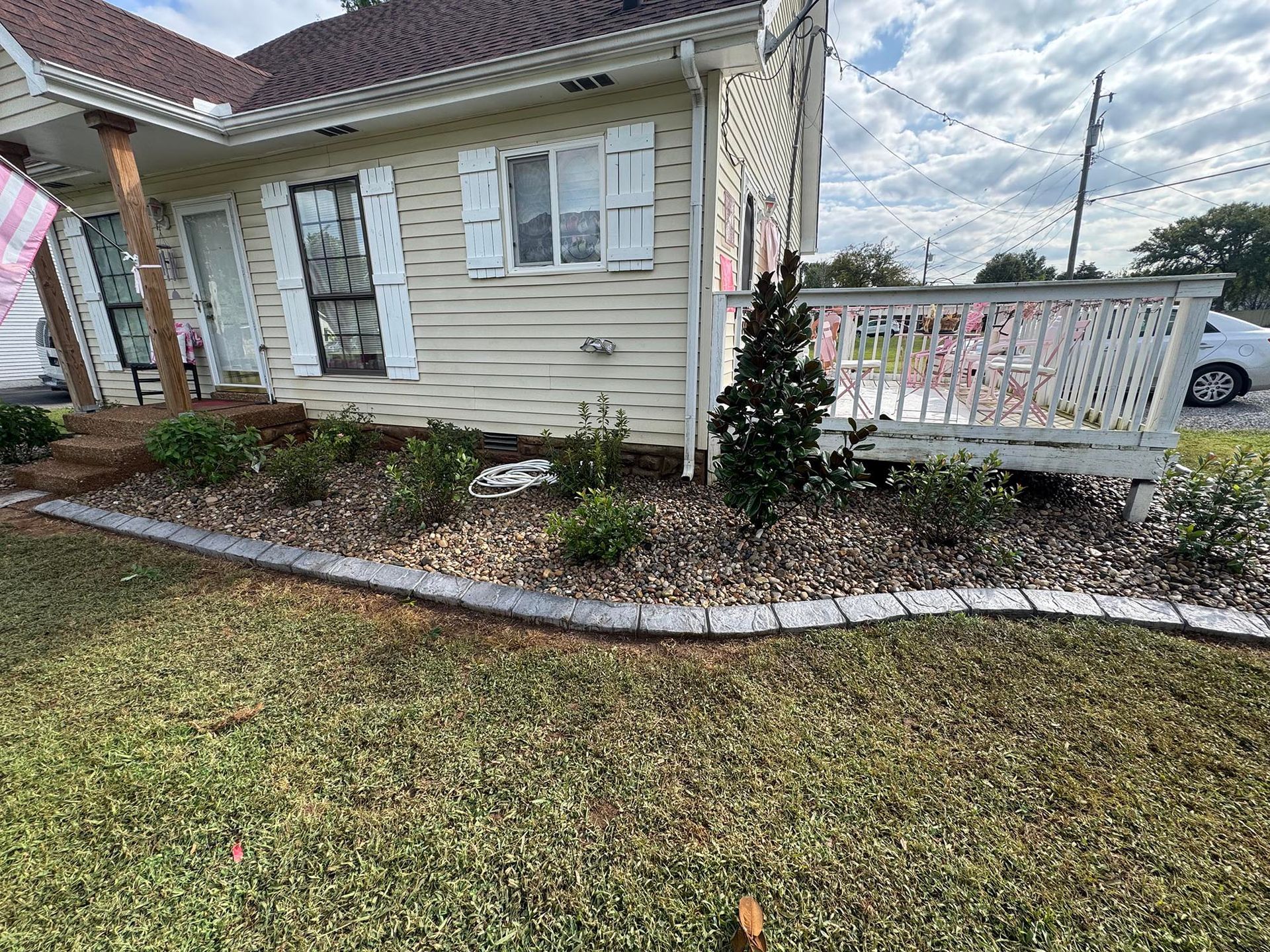 A tan house with a landscaped front yard. Gray curbing surrounds the flower bed.
