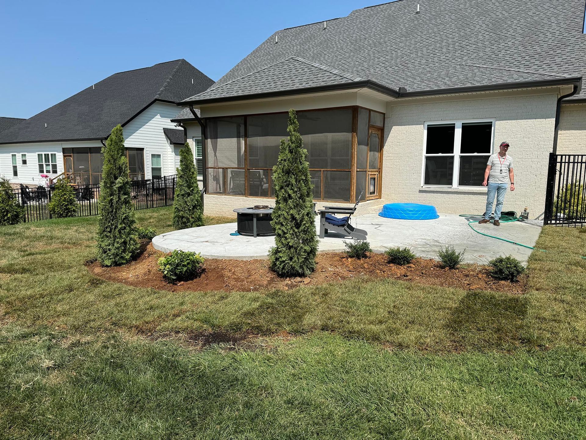 Backyard patio with landscaping and a person watering plants.