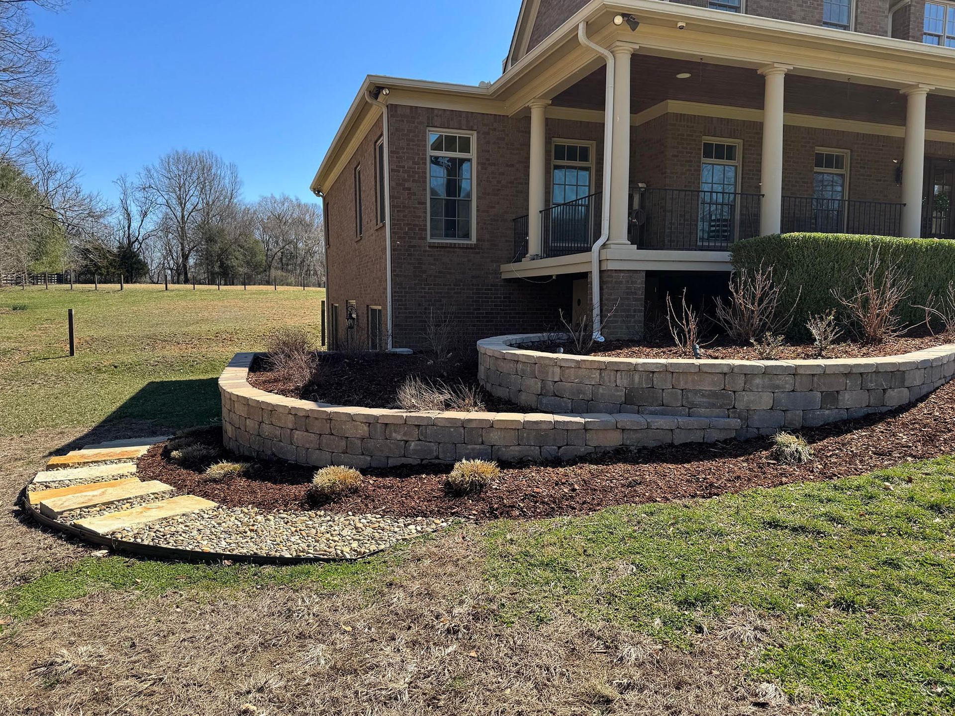 Stone terraced landscaping in front of a brick house with a porch, sunny day.