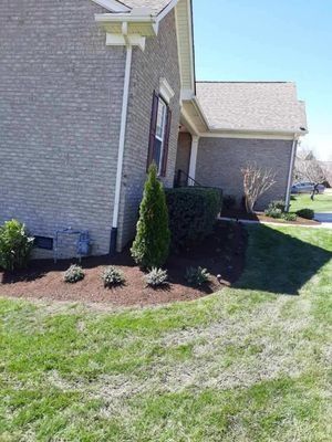 A brick house with green grass, flower beds, and a dark roof. Sunny day.