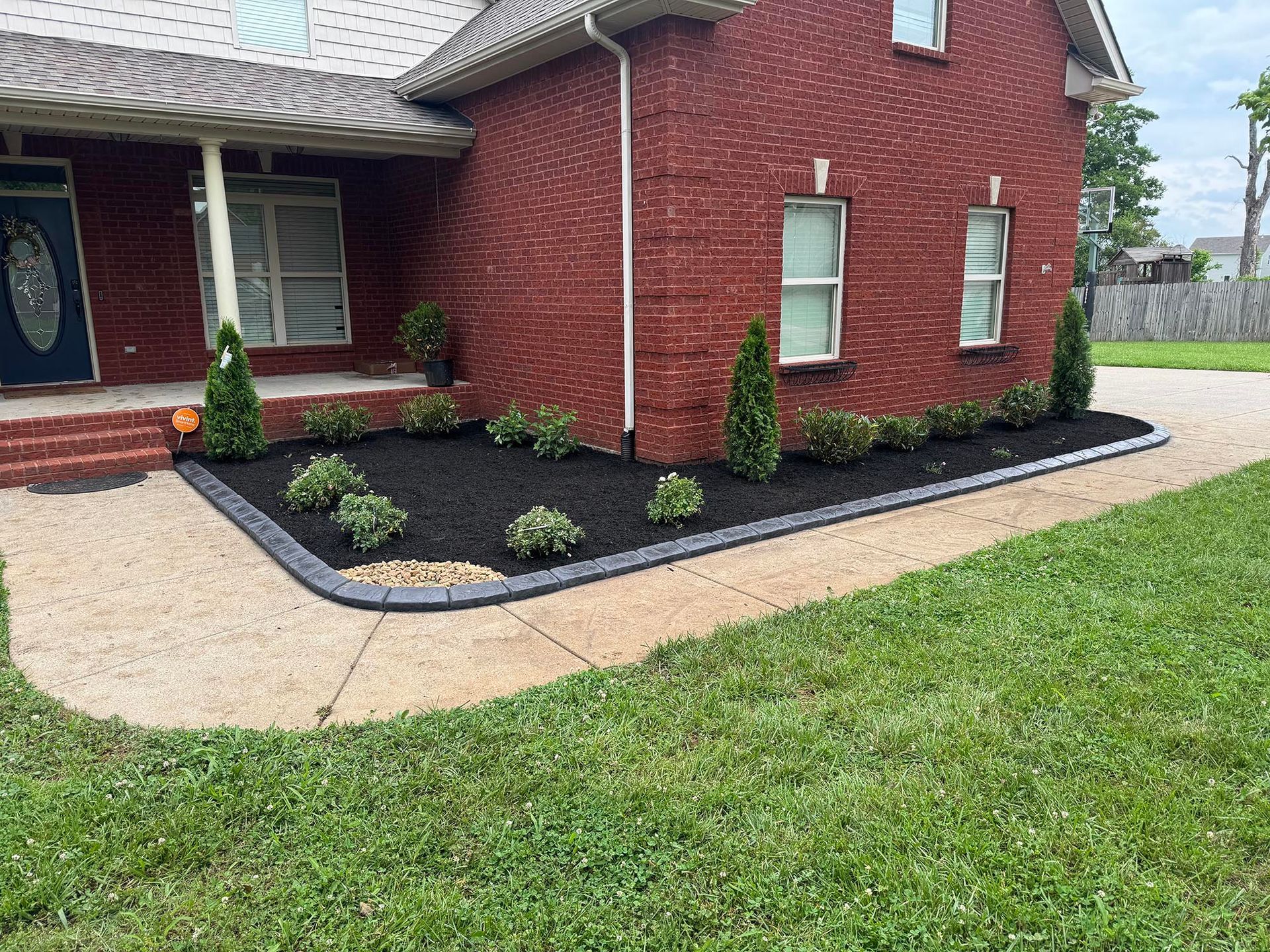 Red brick house with landscaped flower bed and gravel walkway.