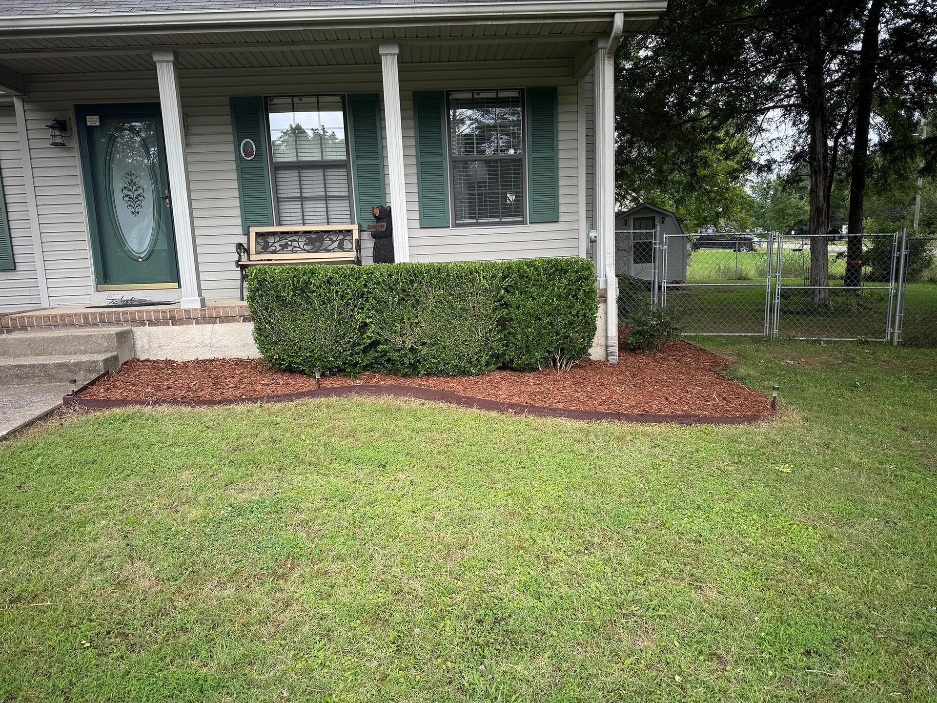 House front with green lawn, a trimmed hedge, and mulch border.