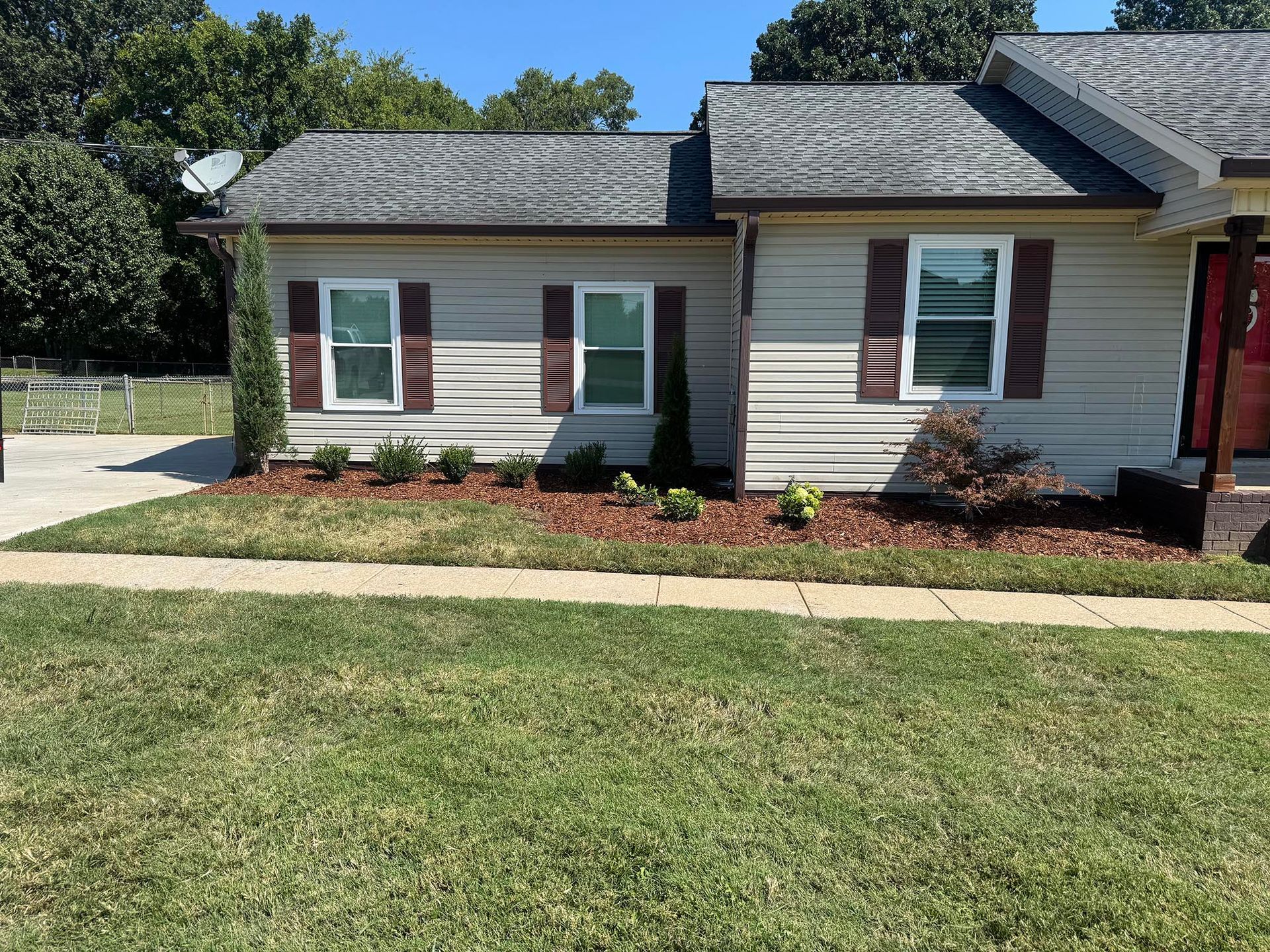 House with tan siding, brown shutters, and a landscaped front yard with green grass and mulch.