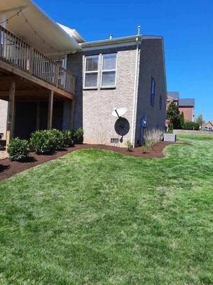 Side view of a brick house with a deck, landscaping, and a clear blue sky.