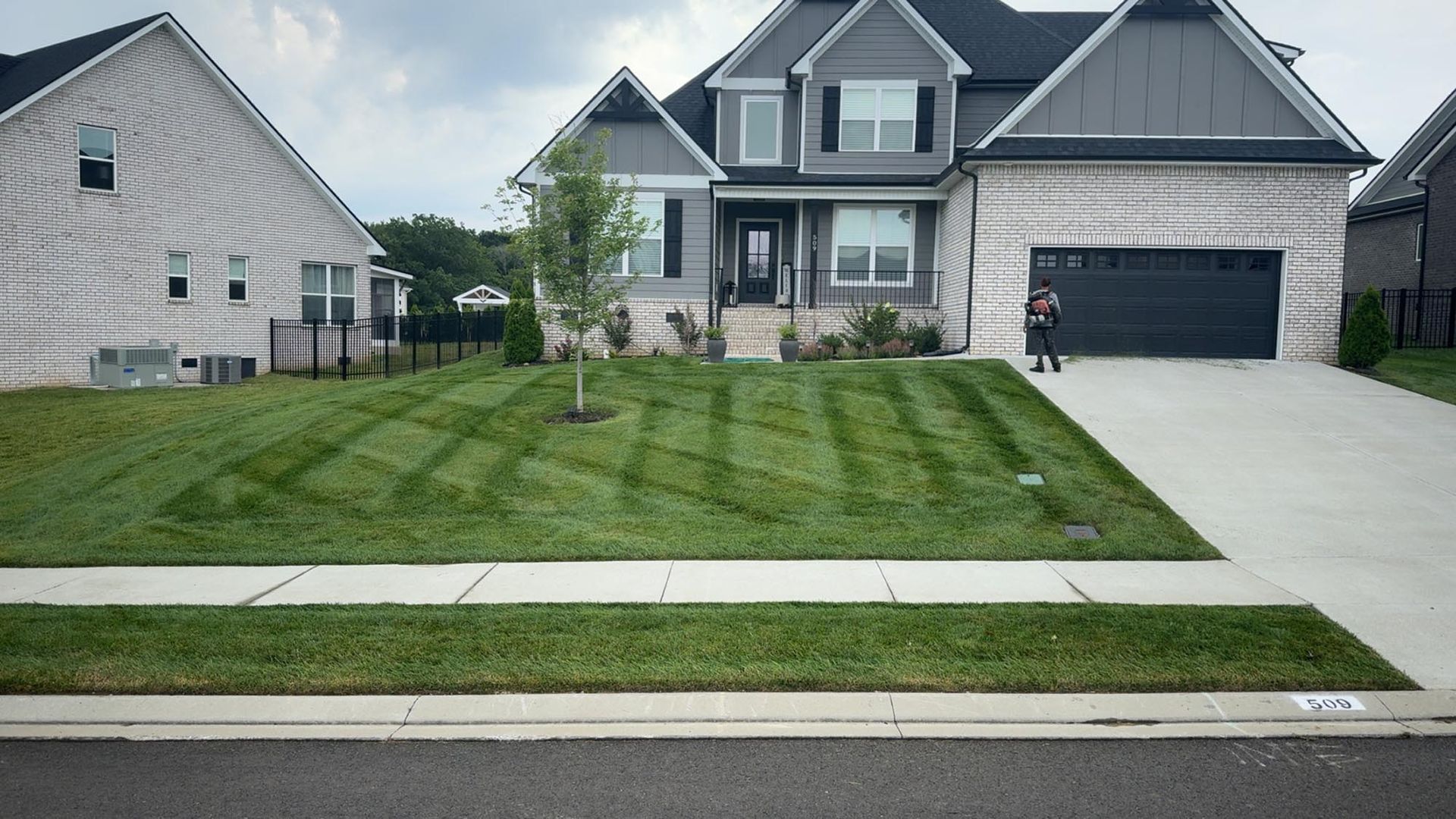 A house with striped lawn and a person standing on the driveway.