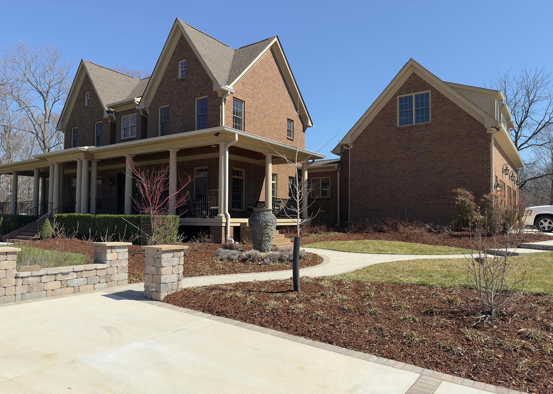 Brick house with a wraparound porch and detached garage on a sunny day.