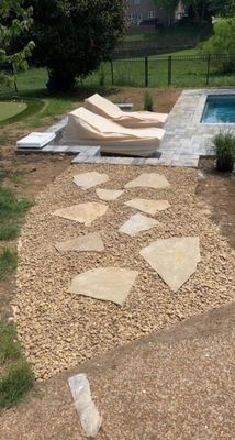A stone path leads to a pool area with lounge chairs on a sunny day.