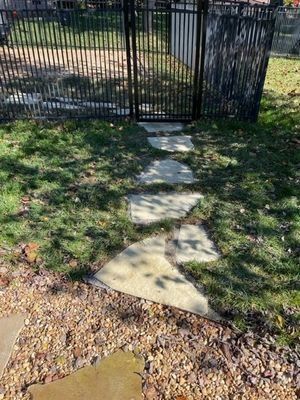 Stone pathway leading to a black metal gate, set in a grassy yard.