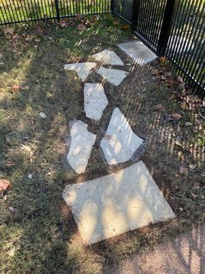 Stone stepping stones laid out on a grassy area next to a black metal fence.