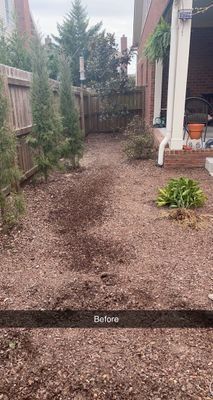 Backyard with freshly tilled soil, small trees, fence, and partial view of a porch.