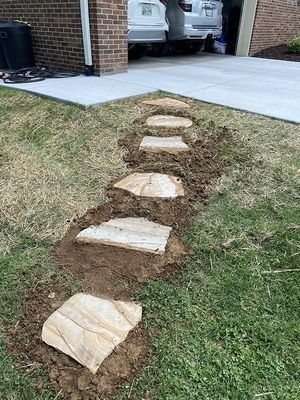 A stone pathway being built on a grassy lawn leading to a garage.