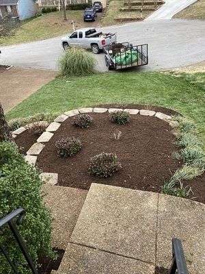 Landscaped front yard with steps, stone-edged flower bed, and a truck with a trailer.