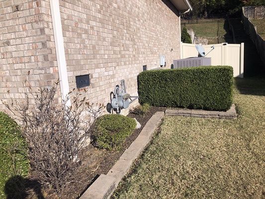 Brick building exterior with a trimmed bush, air conditioner, and lawn.