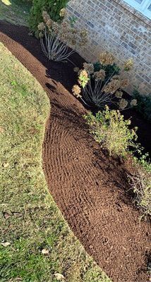 Freshly mulched flower bed with brown mulch beside a building wall and lawn.