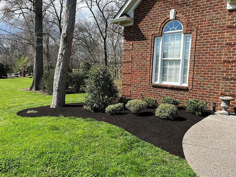 Red brick house with a curved black mulch bed, green grass.