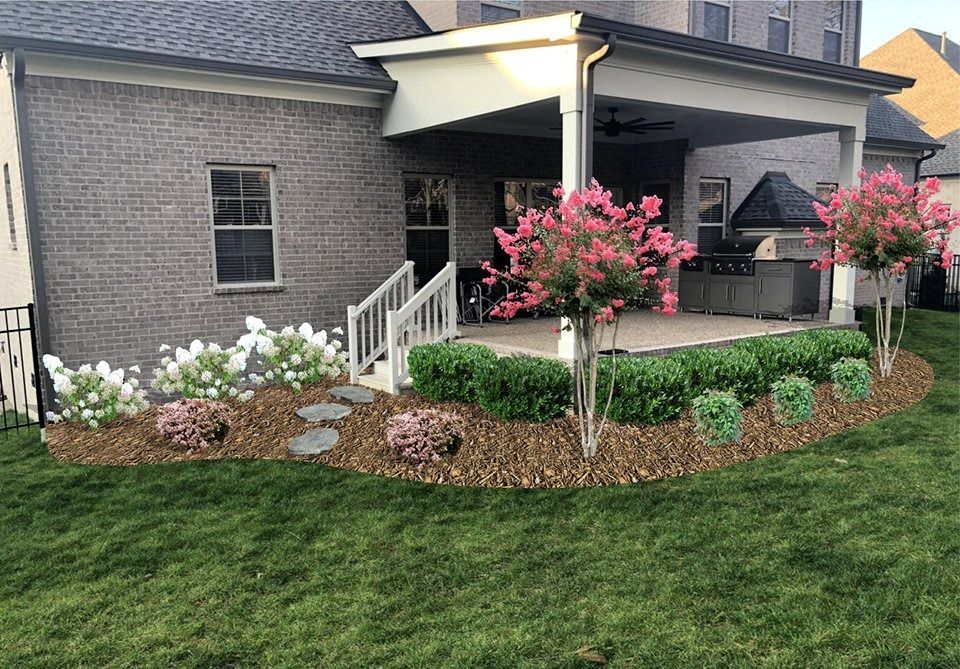 Backyard patio with flowerbeds, lawn, and brick house.