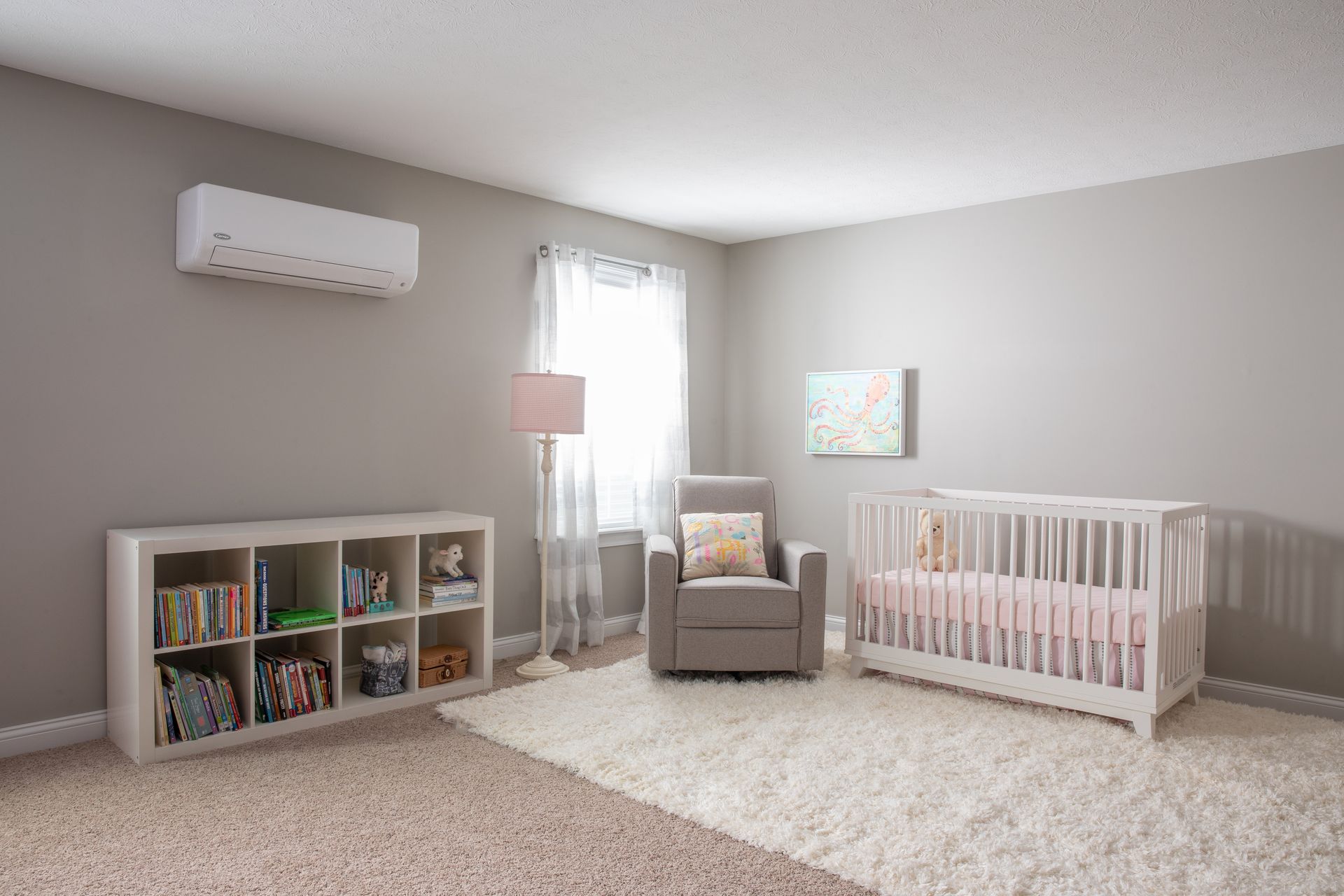 A nursery with a white crib, a gray armchair, a cube storage shelf, a floor lamp, and an AC unit on a light gray wall.
