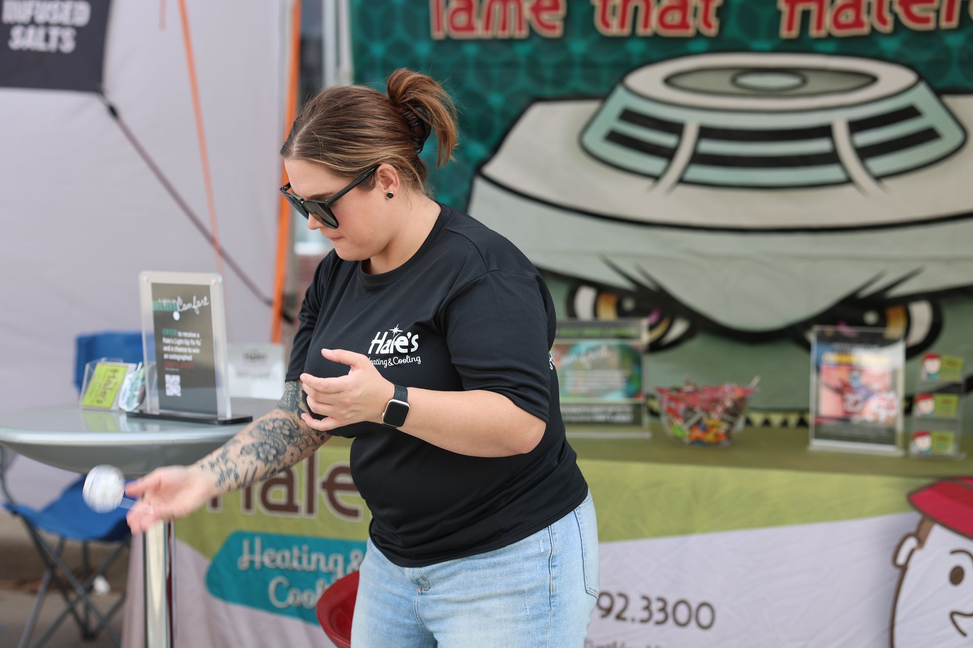 A person in a black branded t-shirt tosses a ball near a booth with an HVAC company logo and 
