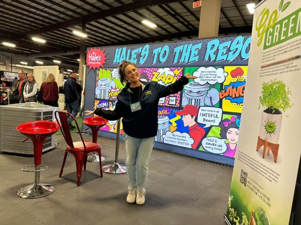 A person smiles and poses in front of a comic-book-style trade show booth next to a 