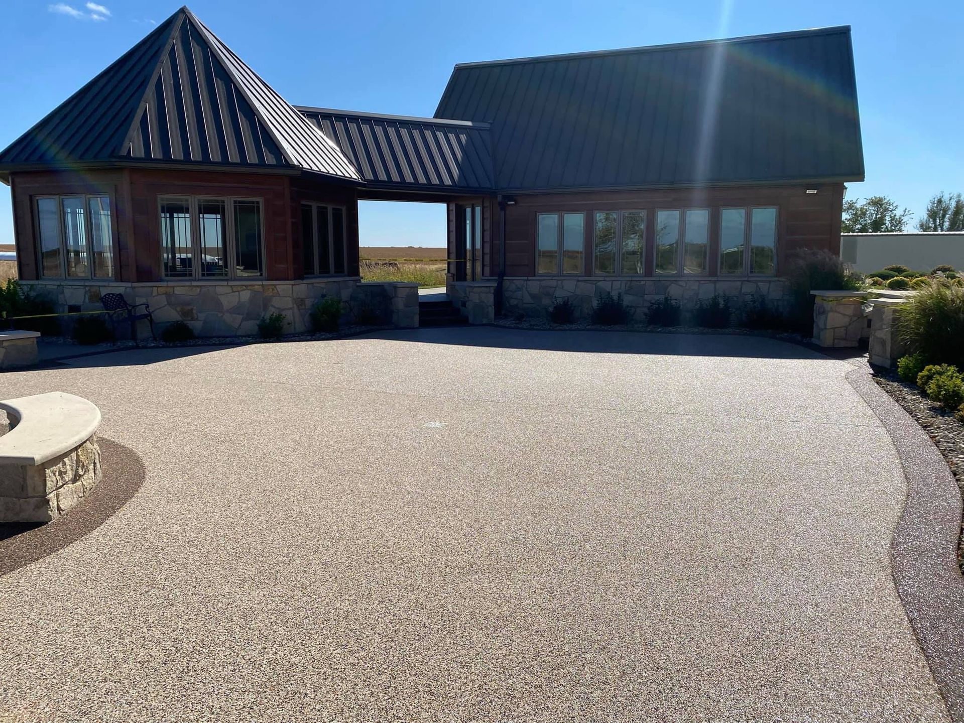 A wide-angle view of a custom home with a stone foundation, metal roof, and large windows bordering a paved courtyard