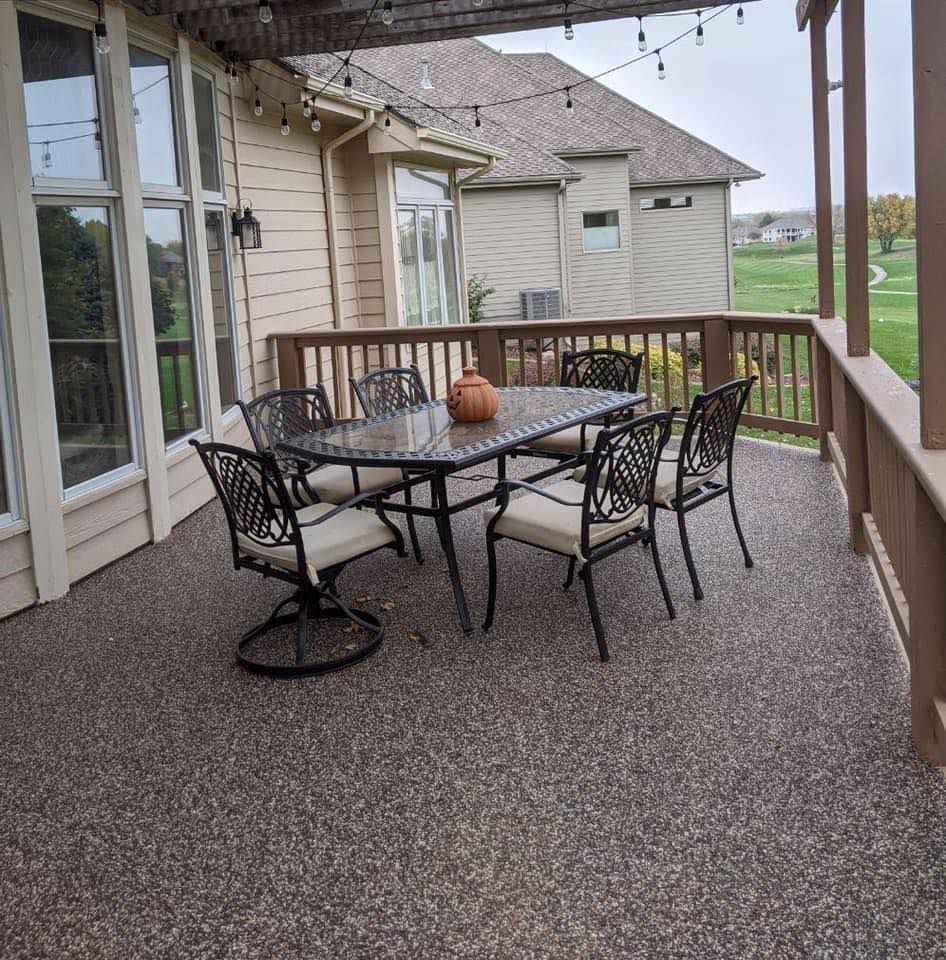 A patio with a metal dining table and four chairs, featuring a speckled textured floor and wood railings
