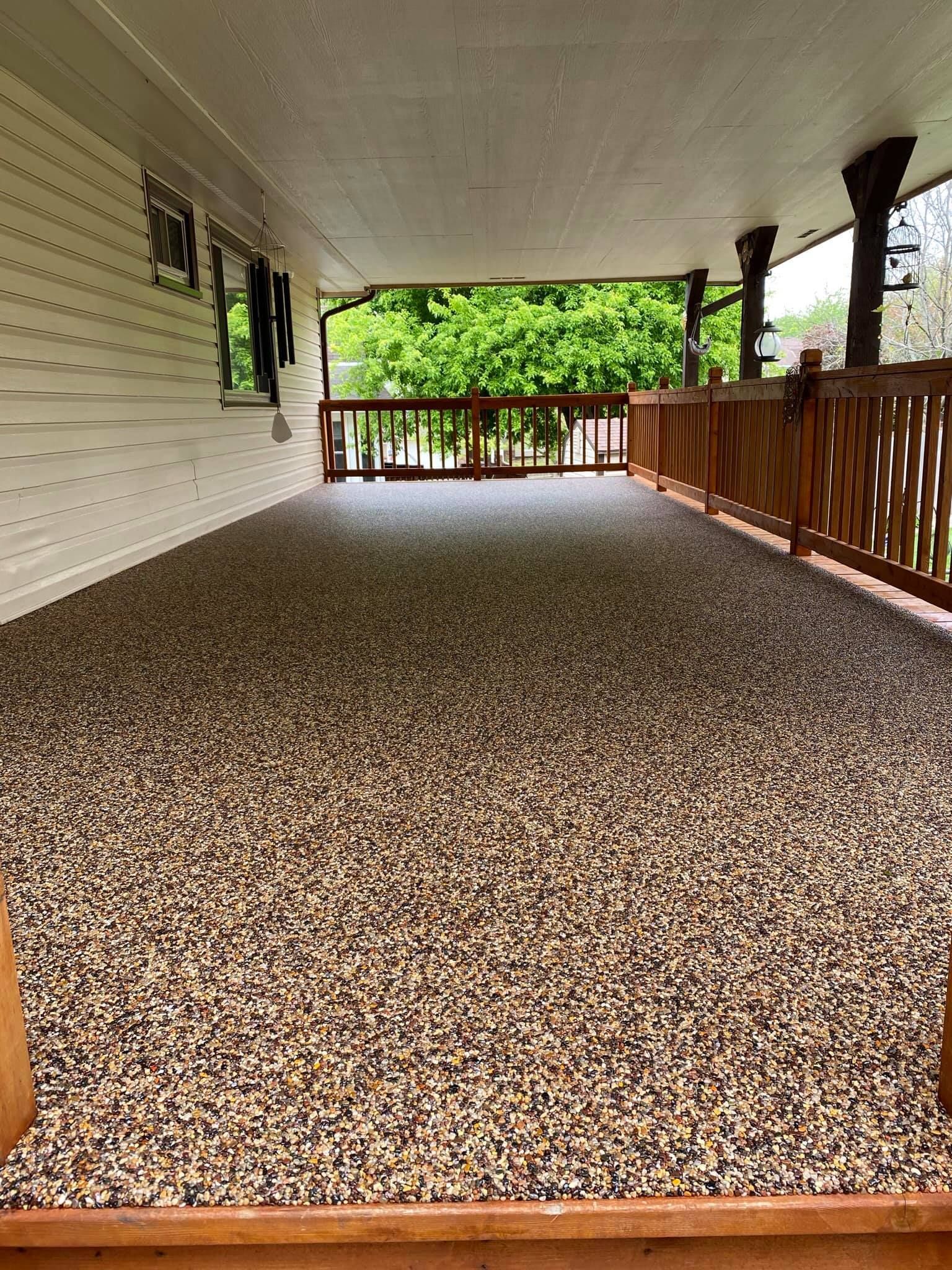 A covered porch features a floor with a multi-colored stone-flecked epoxy finish and wooden railings