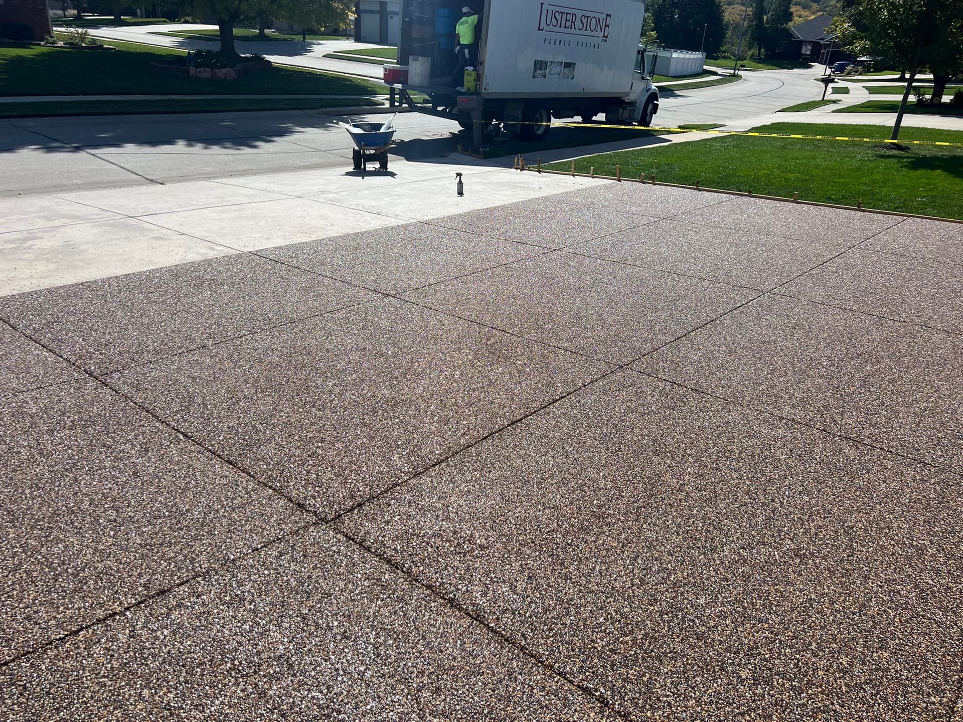 A residential driveway undergoing renovation, featuring exposed aggregate concrete and a work truck parked nearby