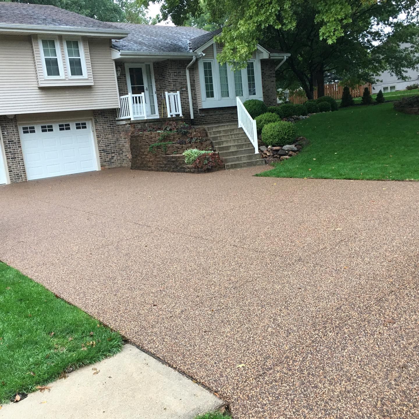 A modern house with a stone-accented facade, a two-car garage, and a textured pebble driveway leading to the front stairs