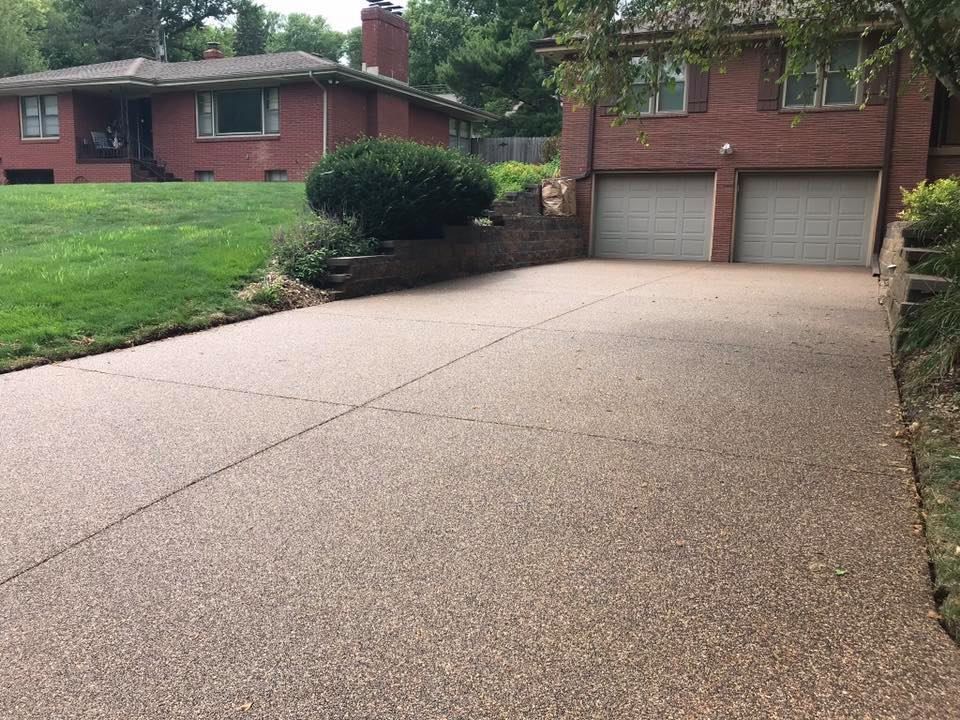 A concrete driveway leads to a two-car garage attached to a red brick house with a green lawn