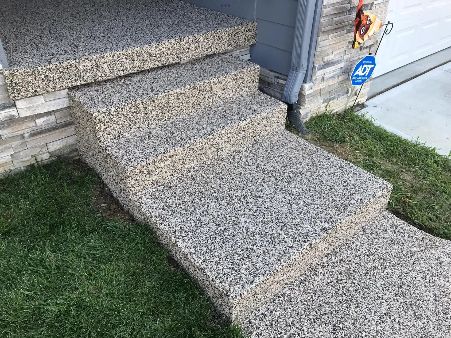 Three outdoor concrete steps with a speckled, stone-textured finish leading to a residential porch.