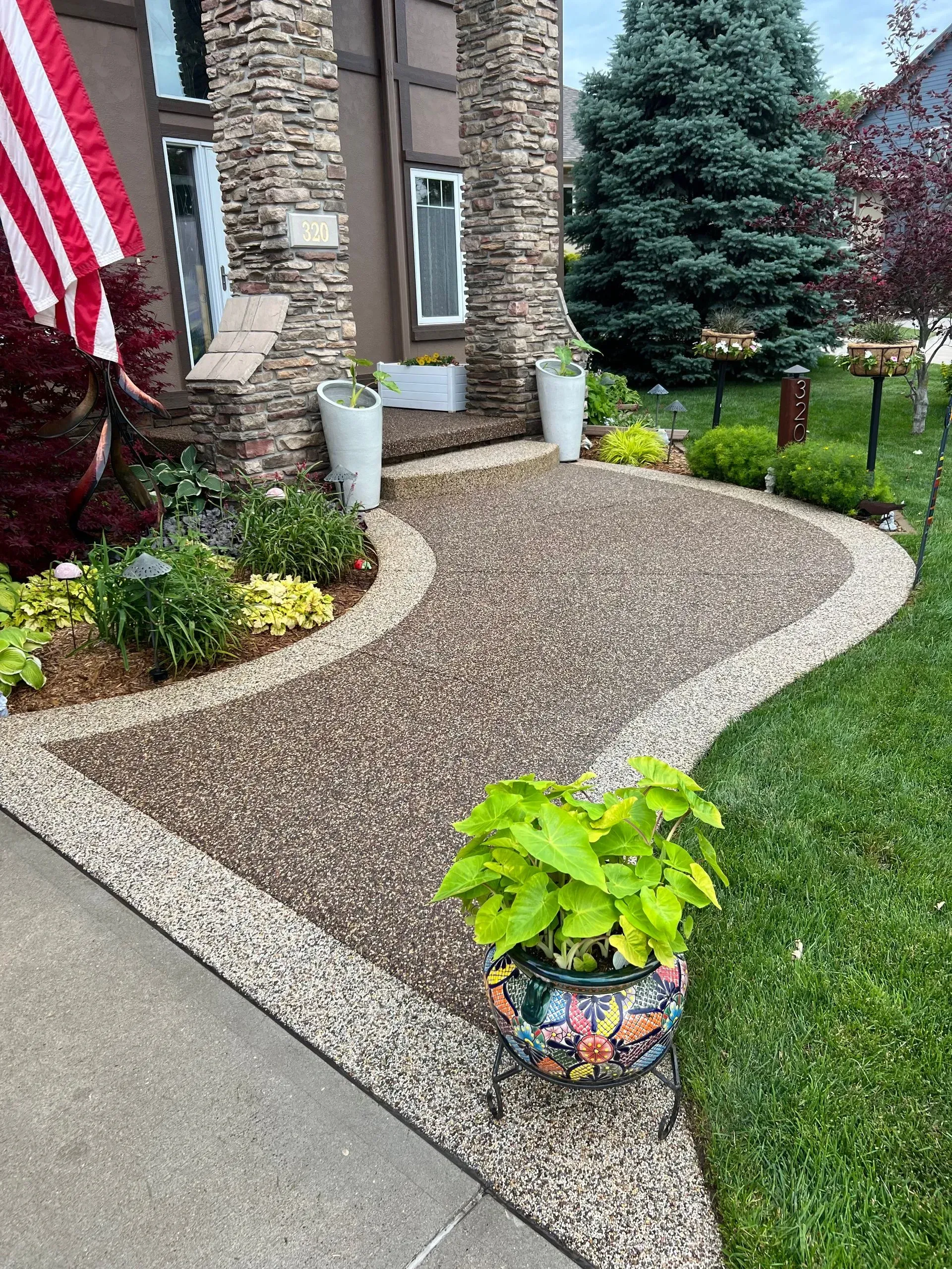 A curved pebble-covered walkway leads to a home entrance with stone siding, white planters, and a potted plant in front.