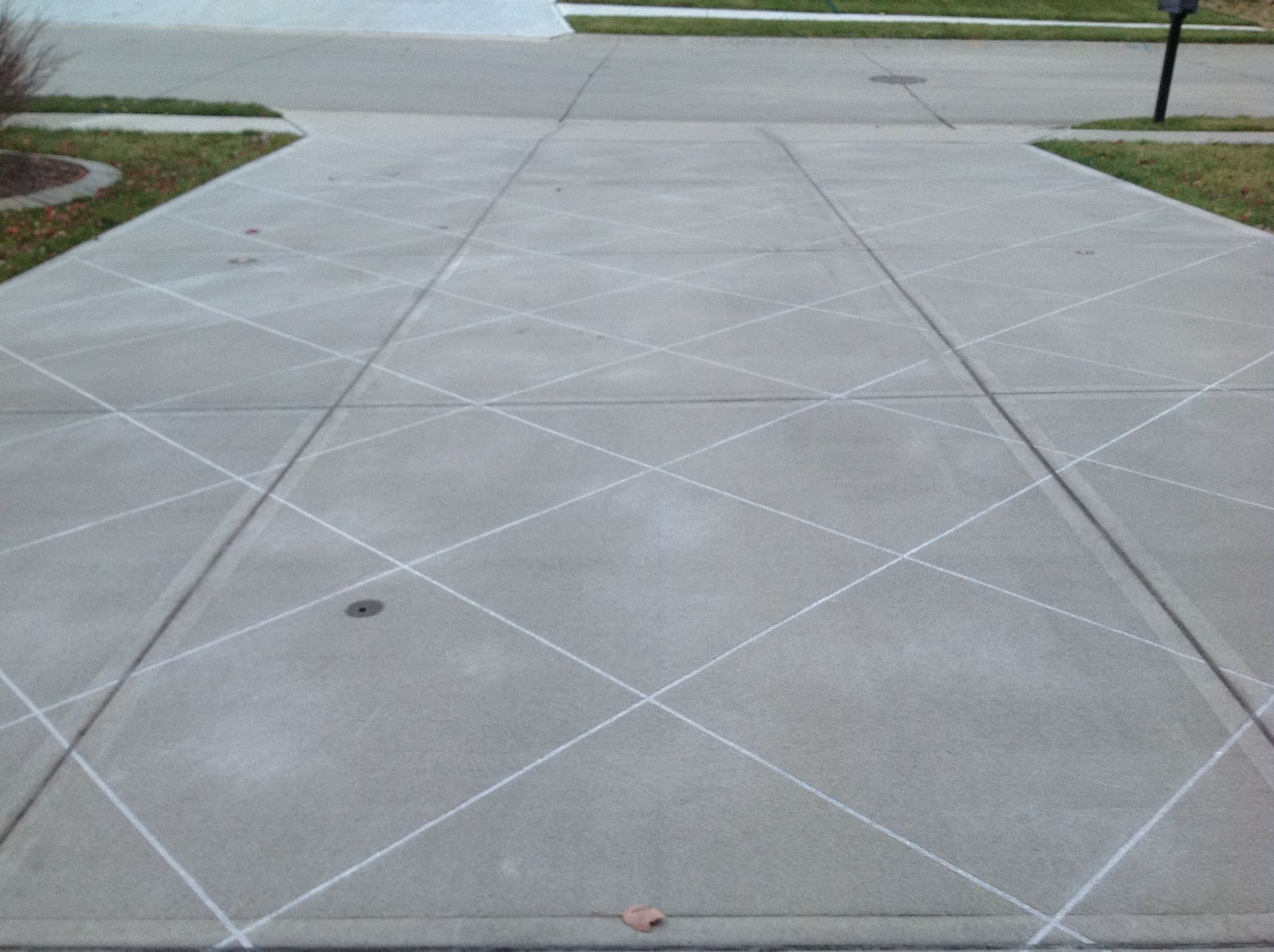 A concrete driveway featuring decorative, white, diagonal cross-hatch lines etched into the surface.