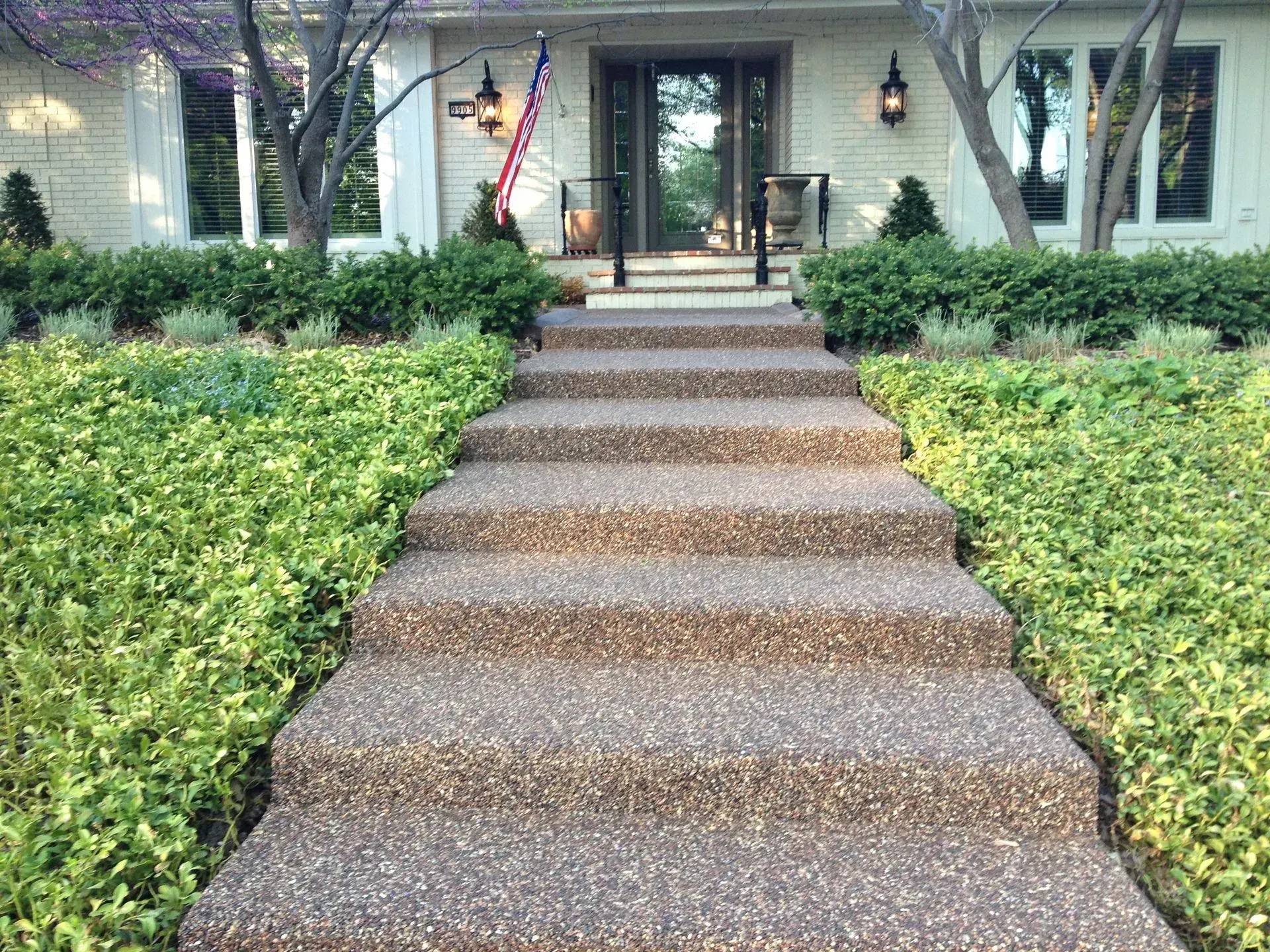 A set of wide, aggregate concrete steps leading up to the front entrance of a house with light-colored siding.