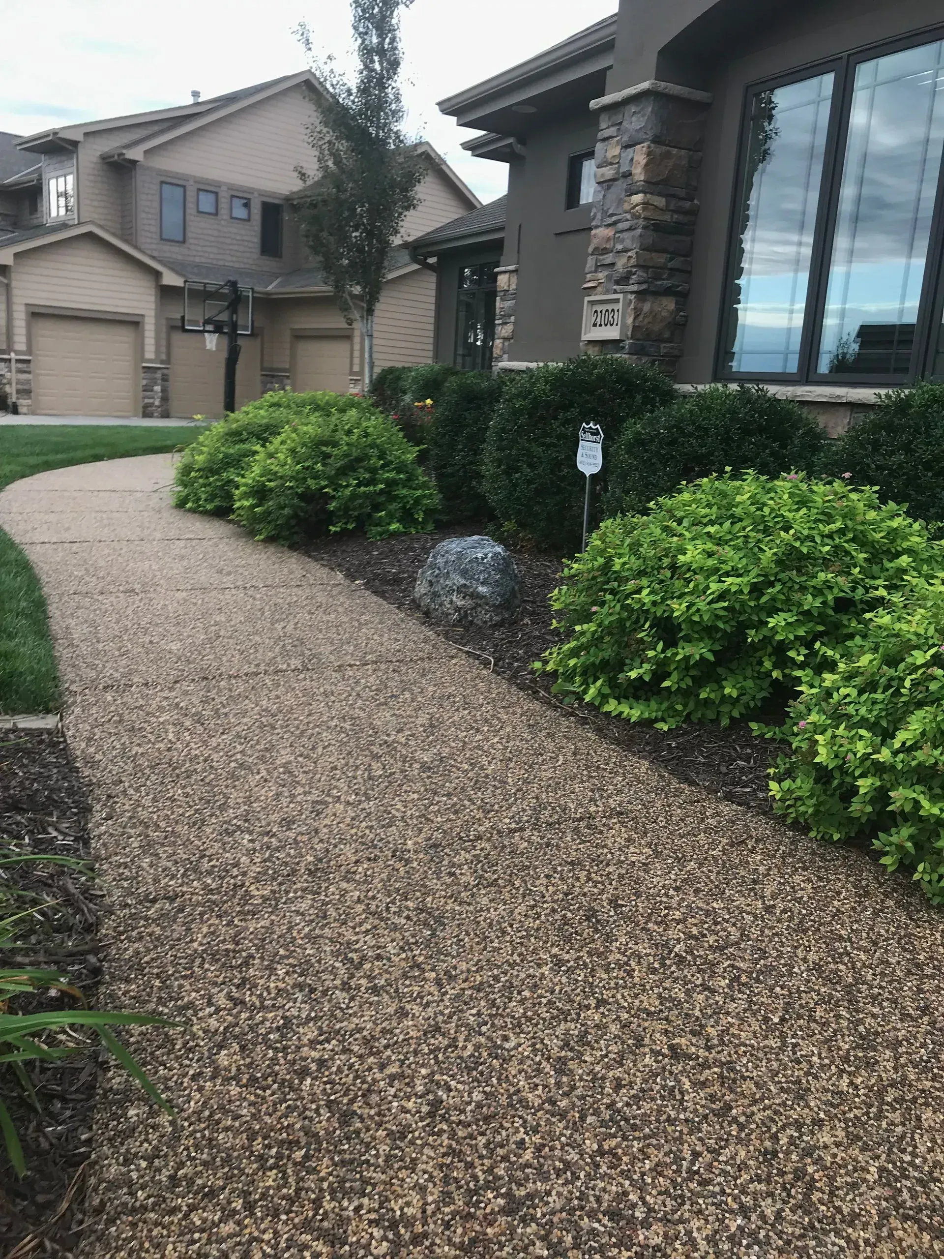 A gravel walkway leads toward a house entrance with landscaping shrubs and a gray stone accent.
