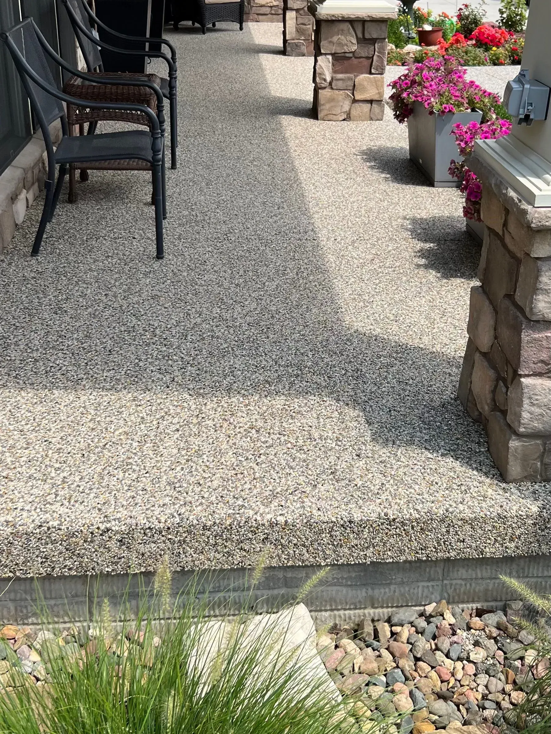 A stone-textured porch featuring two black chairs and a planter box with pink flowers next to a stone pillar.