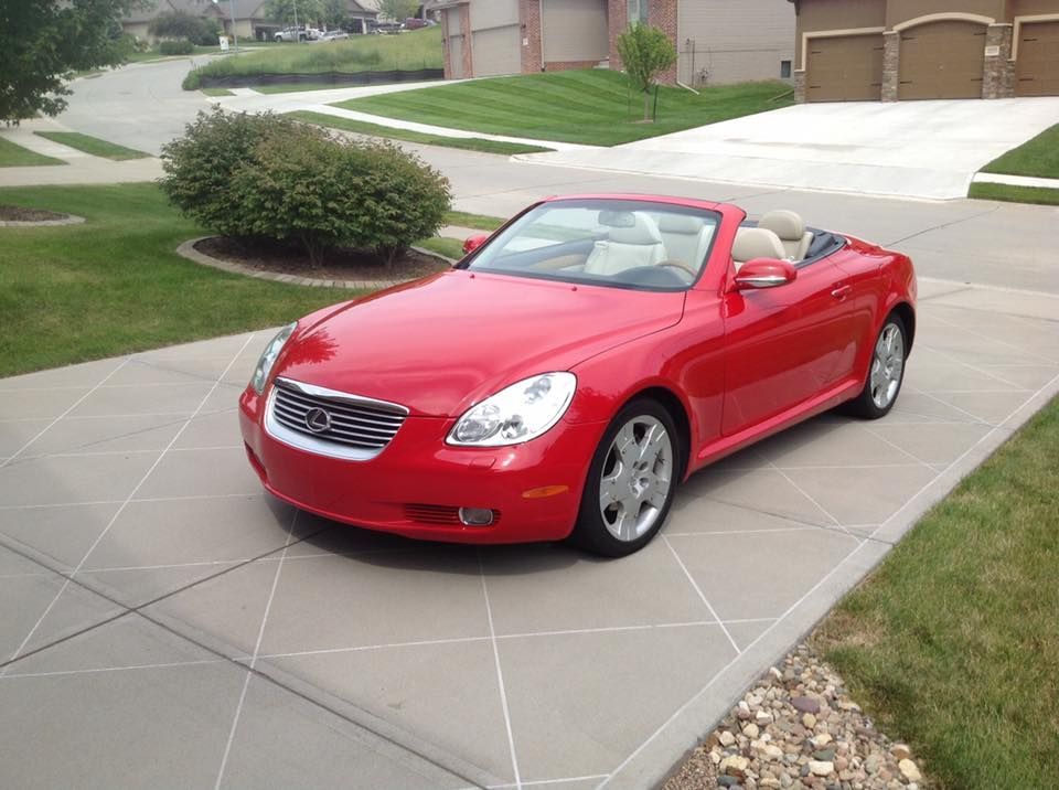 A red convertible car parked on a suburban concrete driveway with a diamond-patterned design.