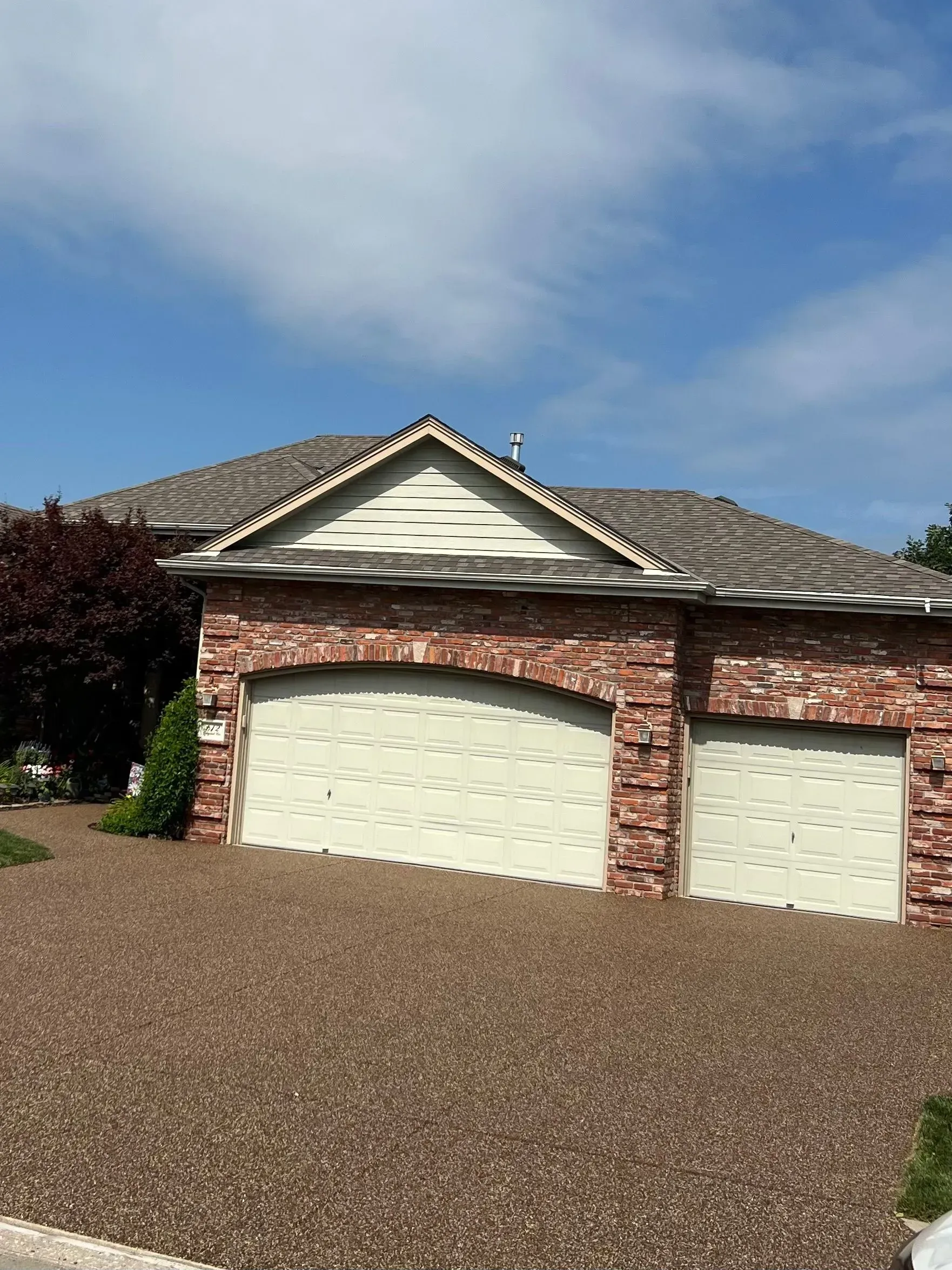 A single-story brick house with a two-car garage under a gabled roof, set behind a front yard covered in brown gravel.