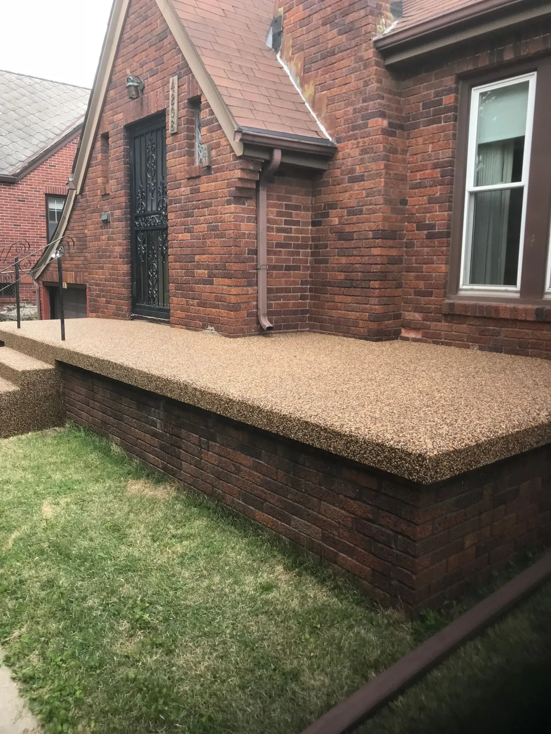 A brick house features a newly resurfaced, textured pebble-aggregate front porch and step.