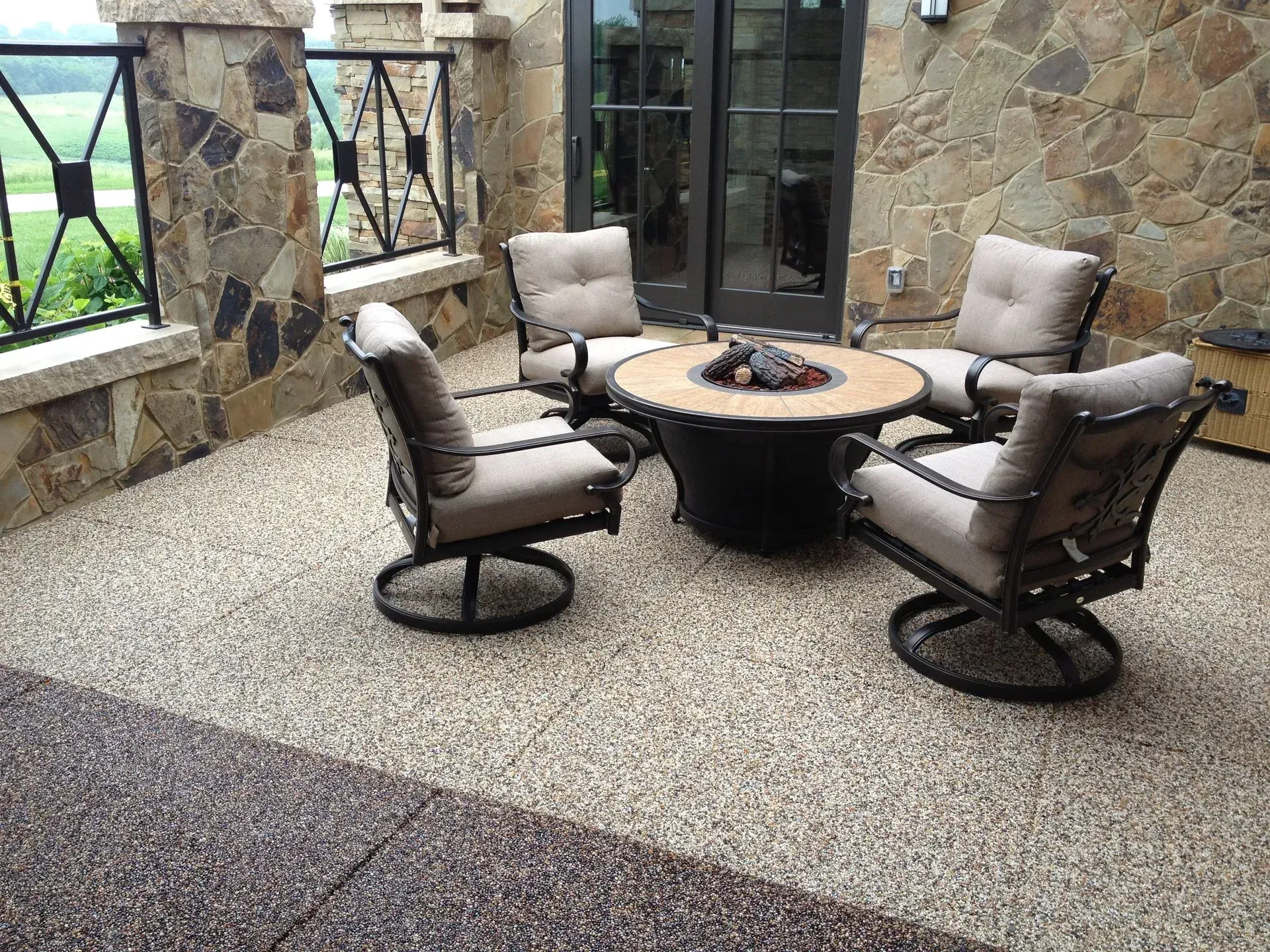 A patio featuring four swivel chairs with beige cushions arranged around a round fire pit on a gravel surface.