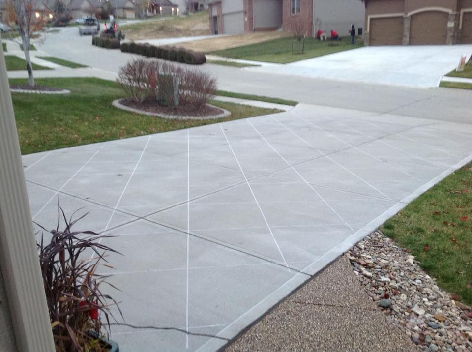 A residential concrete driveway featuring decorative, diagonal, saw-cut grid lines in a suburban neighborhood.