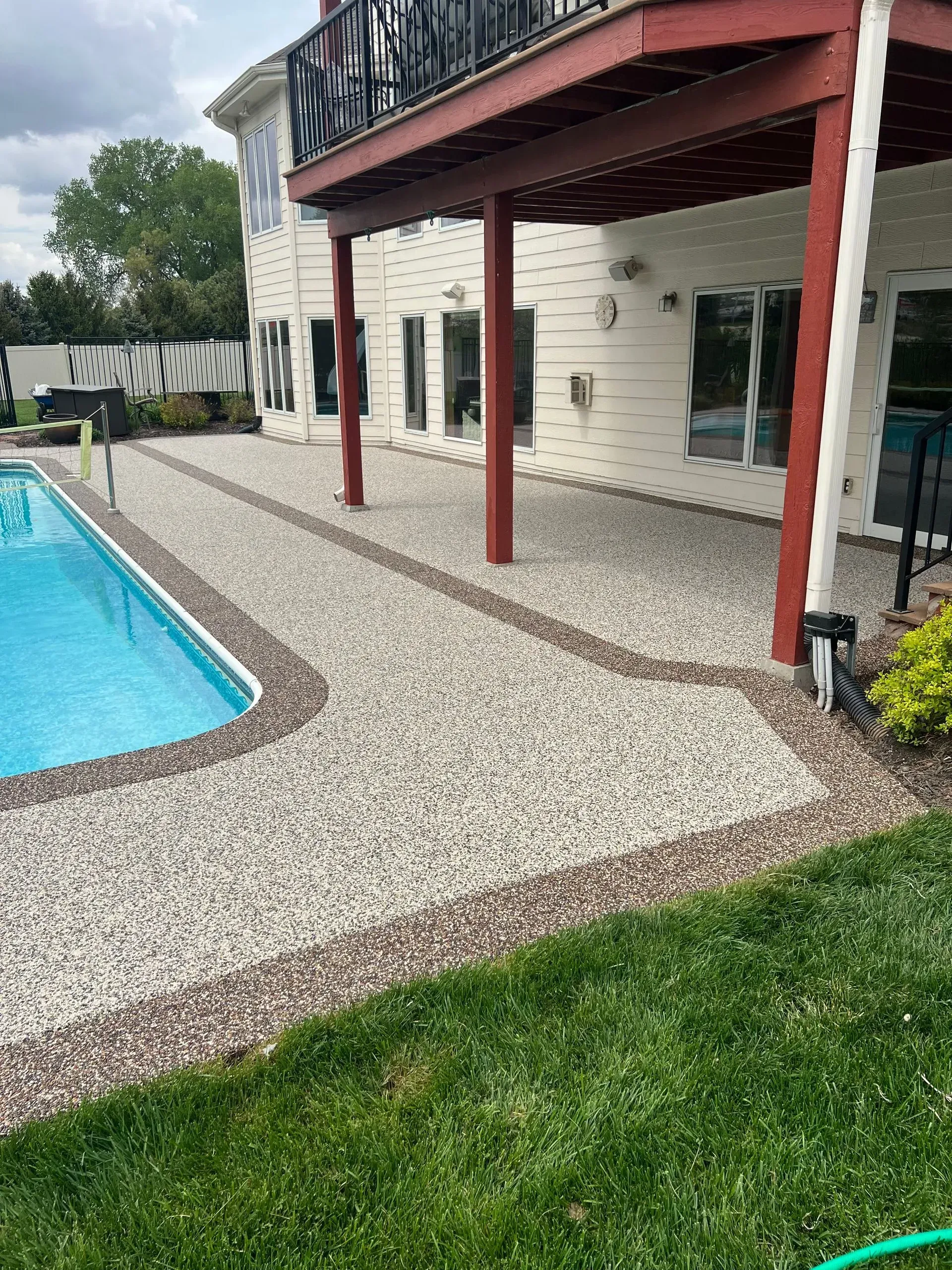 An outdoor swimming pool with a stone patio and a raised wooden deck attached to a house.